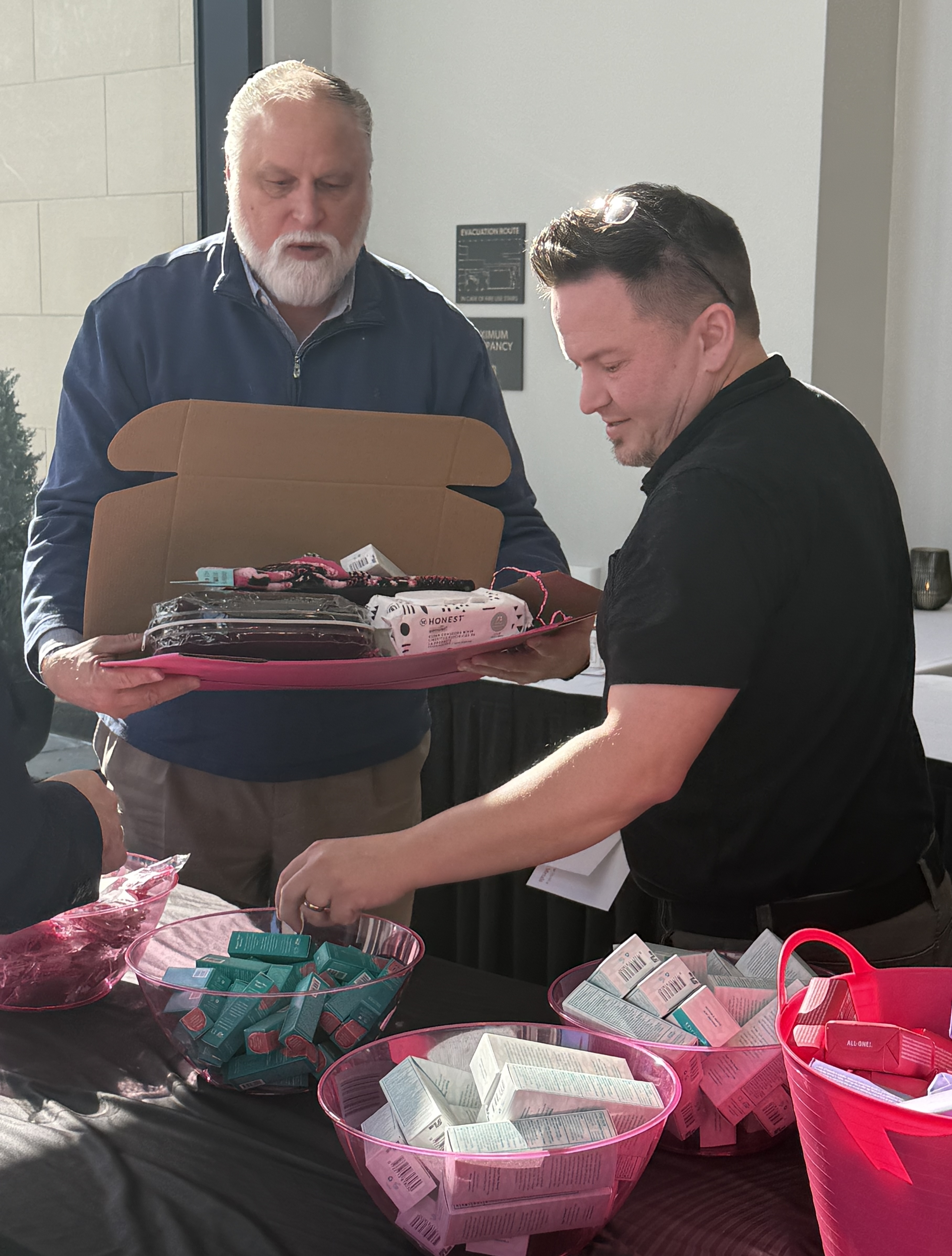 Two male sales representatives help add items to a Breastie Box