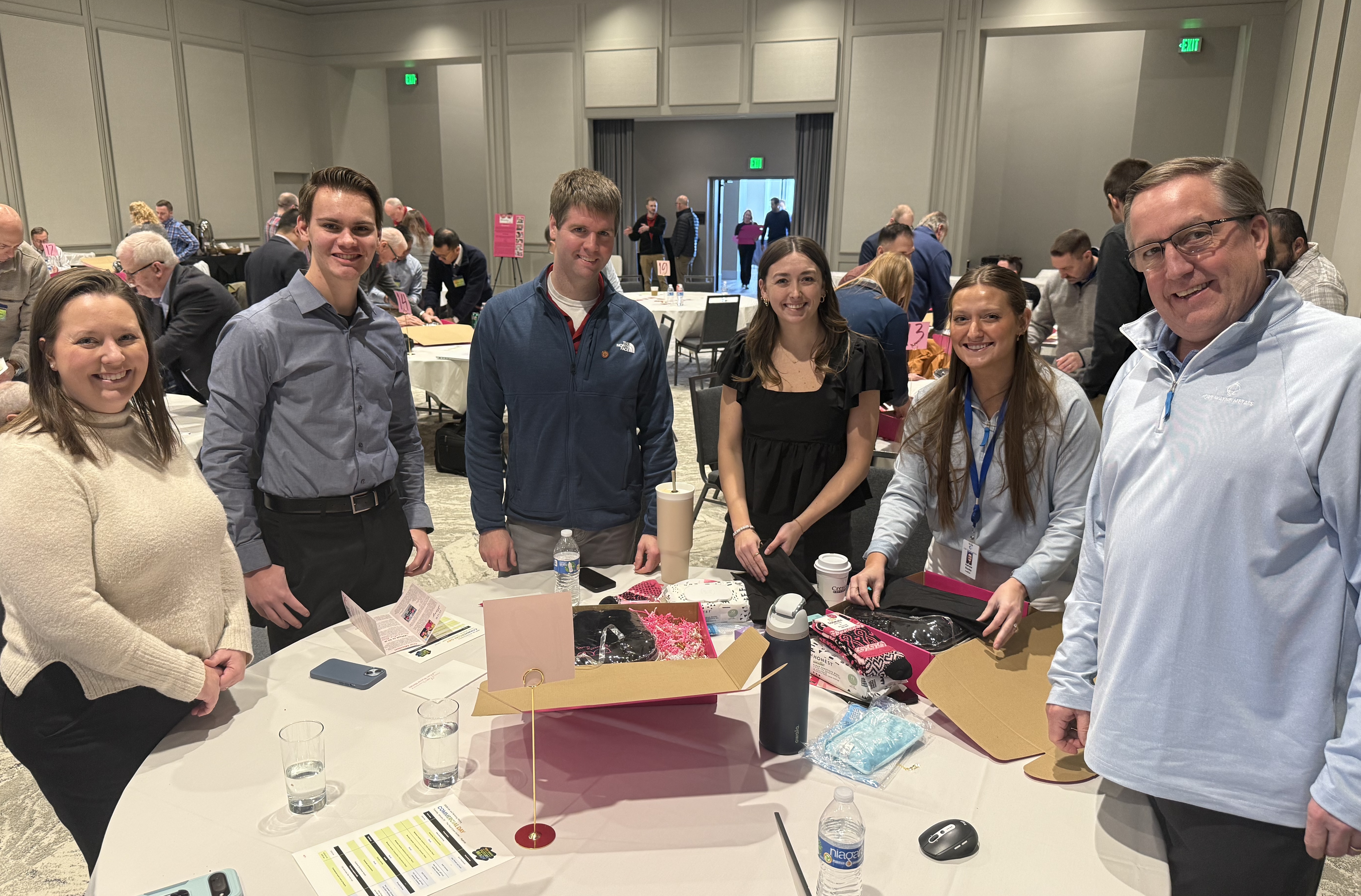 A group of customer service representatives stand around a table helping assemble a Breastie Box